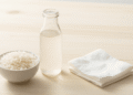 Agua de arroz leitosa num frasco de vidro com arroz branco e disco de algodao ao lado