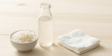 Agua de arroz leitosa num frasco de vidro com arroz branco e disco de algodao ao lado