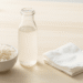 Agua de arroz leitosa num frasco de vidro com arroz branco e disco de algodao ao lado