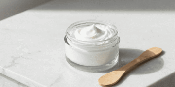 Tigela de base Croda cremosa branca ao lado de pote de creme pronto sobre marmore claro