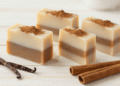 Sabonetes de canela e baunilha em camadas creme e marrom polvilhados com canela e paus de canela ao lado