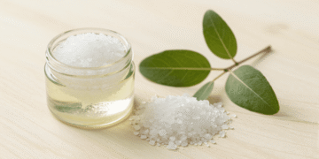 Esfoliante de sal grosso com tea tree para os pes num pote com sal grosso e ramo de melaleuca ao lado