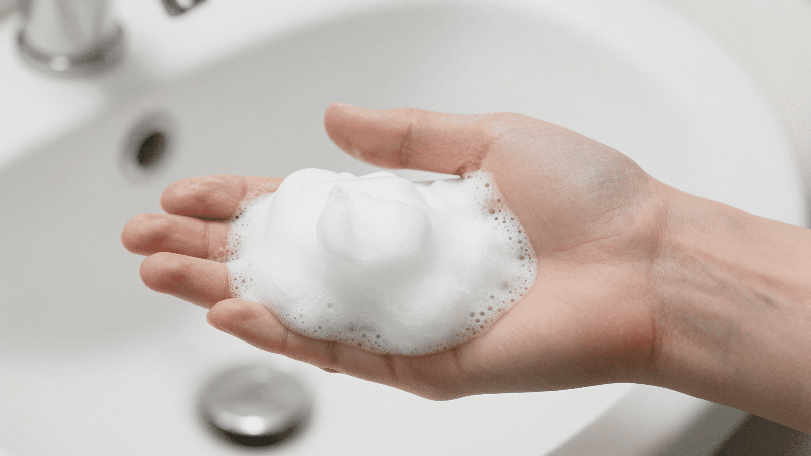 Espuma de limpeza facial natural branca e cremosa na palma da mao sobre a pia