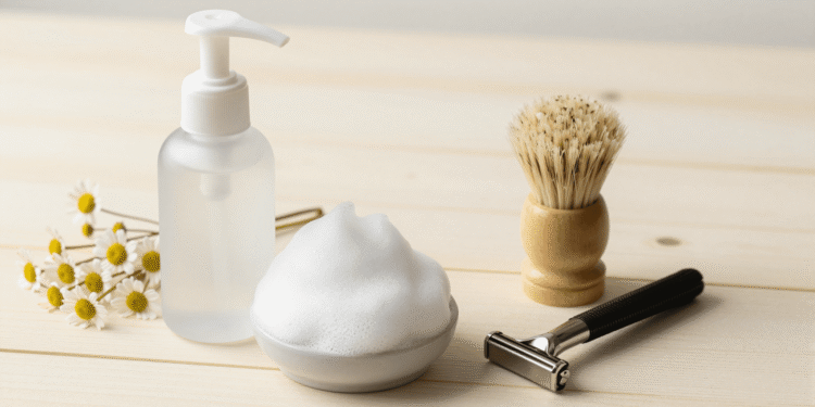 Espuma de barbear caseira num frasco espumador com pincel, aparelho e flores de camomila ao lado