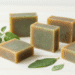 Sabonetes naturais de oregano e neem esverdeados com ramos de oregano e folhas de neem ao lado
