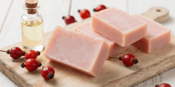 Sabonetes artesanais de rosa mosqueta rosados sobre tabua de madeira com frutos e oleo