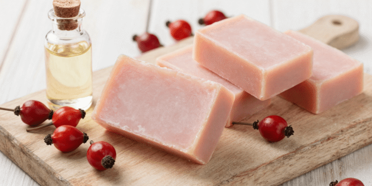 Sabonetes artesanais de rosa mosqueta rosados sobre tabua de madeira com frutos e oleo