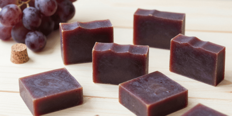 Sabonetes artesanais de vinho cor de vinho tinto com uvas roxas e rolha ao lado