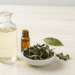 Tonico facial natural num frasco de vidro com folhas de cha verde e oleo essencial ao lado