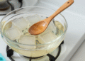 Cubos de base glicerinada derretendo em banho-maria com colher de madeira e formas de sabonete ao lado