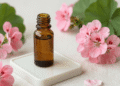 Frasco âmbar de óleo essencial de gerânio cercado de flores de gerânio rosa e folhas verdes
