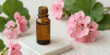 Frasco âmbar de óleo essencial de gerânio cercado de flores de gerânio rosa e folhas verdes