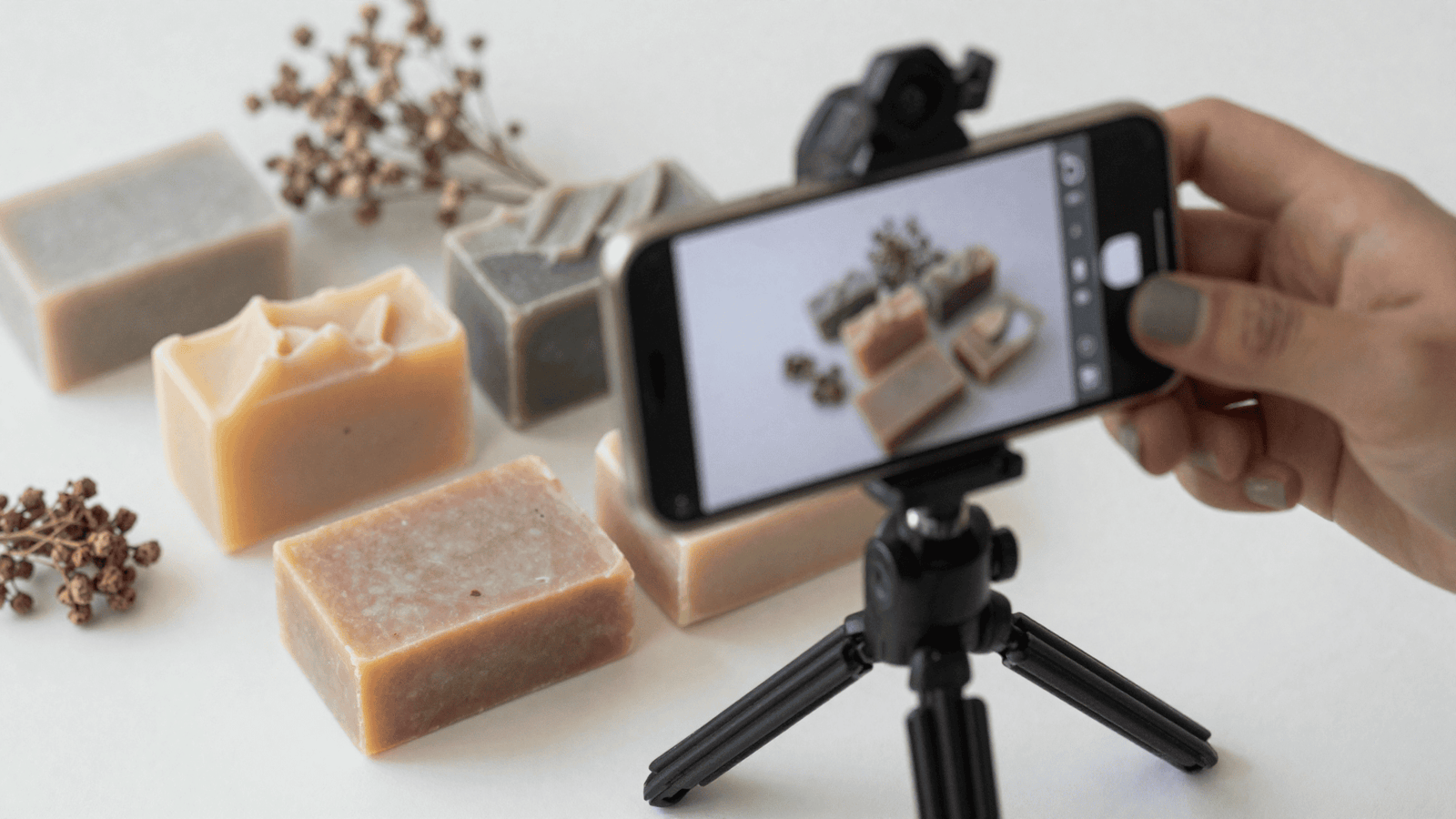 Sabonetes artesanais montados para foto de produto com um celular em um tripé pequeno