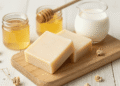 Sabonetes de leite e mel cor de creme em tábua de madeira com pote de mel e jarra de leite
