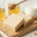 Sabonetes de leite e mel cor de creme em tábua de madeira com pote de mel e jarra de leite