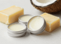 Latinhas de lip balm vegano cremoso ao lado de manteiga de karité, cera vegetal e coco