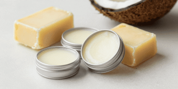 Latinhas de lip balm vegano cremoso ao lado de manteiga de karité, cera vegetal e coco