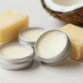 Latinhas de lip balm vegano cremoso ao lado de manteiga de karité, cera vegetal e coco