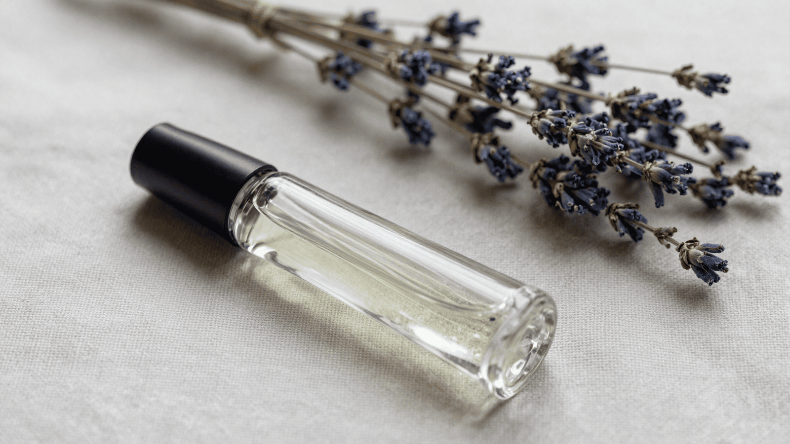 Frasco roll-on de perfume pronto sobre pano de linho com lavanda seca ao lado