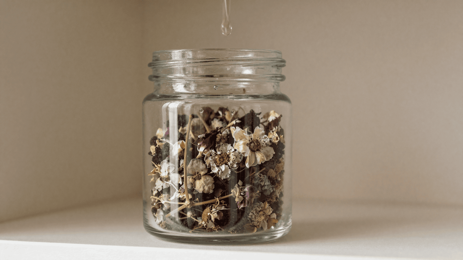 Pote de vidro com pot-pourri de flores secas recebendo gotas de óleo essencial