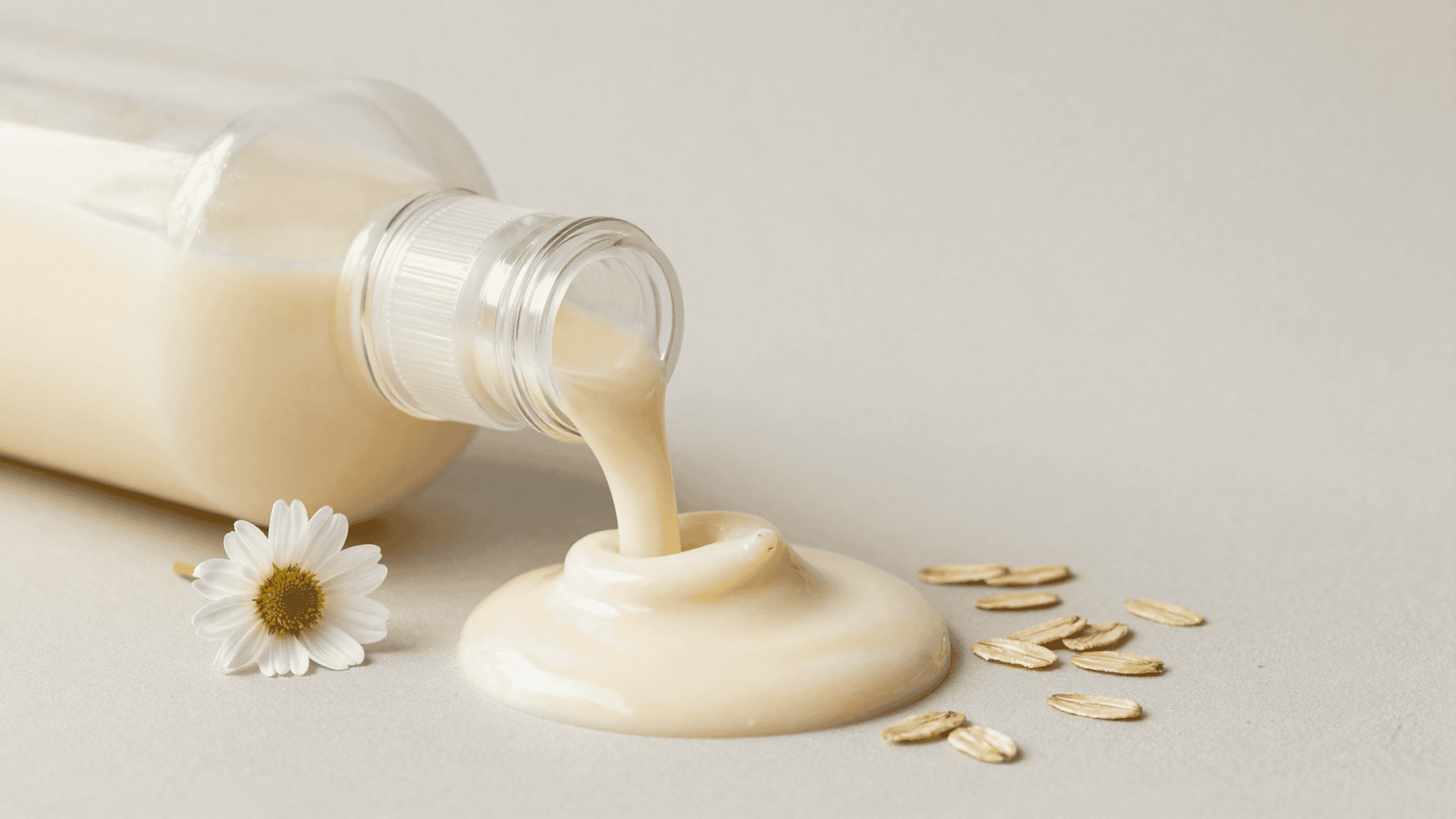 Shampoo de aveia cremoso e claro em um dispenser de vidro com aveia e camomila ao lado